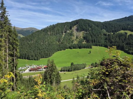 Groene almweide met een dorp diep in het dal ertussen de bomen door – Arbiskogel, Kirchspitze en Stackerlalm, Gerlos